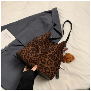 Detailed view of leopard print tote bag with plush dog charm on grey blazer backdrop