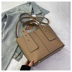 Détail d'un sac seau marron avec motif litchi et rivets dorés sur fond de denim