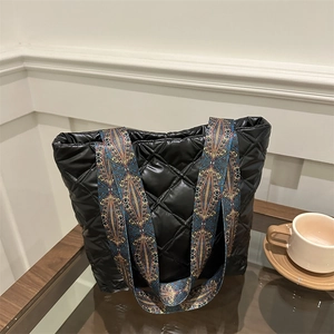 Chic black quilted tote bag with a wide ethnic patterned strap in a stylish cafe setting