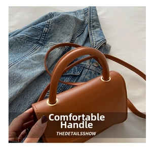 Détails d'un sac à main en cuir marron avec anneaux dorés sur une veste en jean bleue