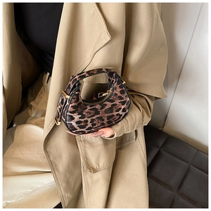 Detail of leopard print crescent bag with gold zippers held against a beige trench coat