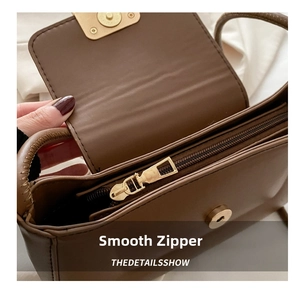 Close-up of smooth gold-tone zipper and magnetic buckle on brown leather shoulder bag