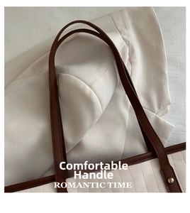 Detail of contrast stitching handle on a beige tote bag with gold hardware accents