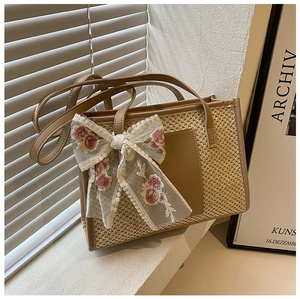 Detail of straw tote bag featuring intricate floral lace bow and premium faux leather trim