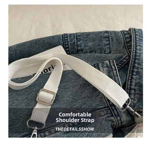 Détail d'une bandoulière tissée blanche réglable avec boucles en métal sur tissu denim