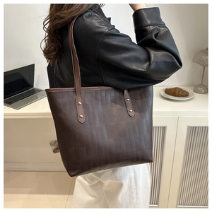 Detail of a dark brown tote bag with brick texture and gold rivets on the shoulder strap