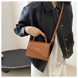 Détail du sac bandoulière en cuir marron avec poignée et lettrage doré sur le rabat