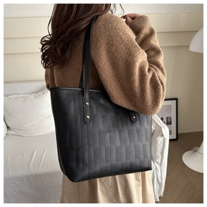 Detail of black tote bag with quilted texture and gold studs shown on shoulder