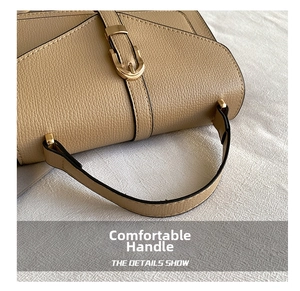 Detailed macro of the textured leather handle and metallic buckle on a beige saddle bag