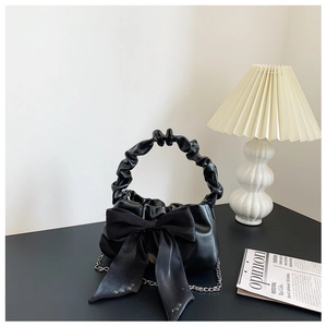 Detail of black handbag with large satin bow, ruched handle and silver chain strap
