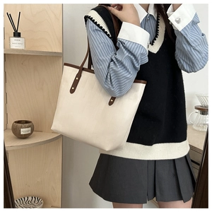 Detail of cream tote bag with textured surface and contrasting brown shoulder straps