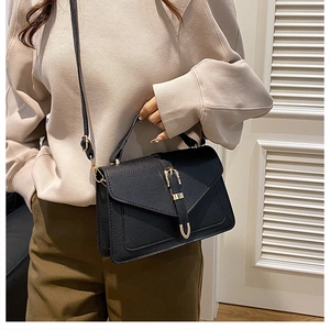 Detail of black pebbled leather crossbody bag with elegant gold buckle on a model