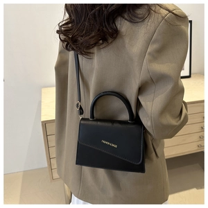 Détail d'un petit sac bandoulière noir en cuir minimaliste avec rabat oblique et texte doré