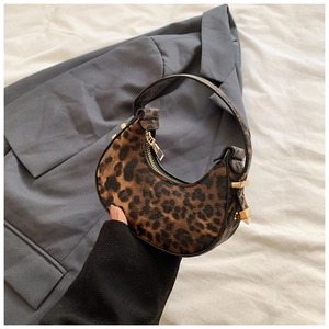 Close-up of leopard print crescent bag with gold zipper and handle in a stylish hand-held shot