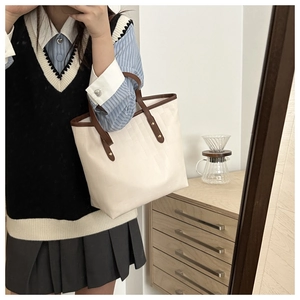 Detail of beige tote bag with woven texture, brown straps and metal rivet accents