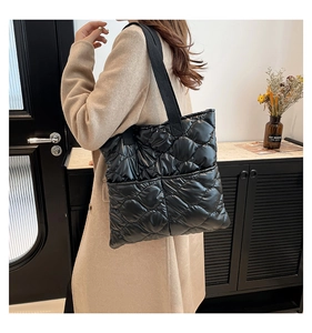Close-up of quilted black tote bag with glossy finish and wide strap on model