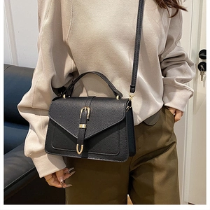 Detail showing a black lychee texture crossbody bag with gold buckle on a model