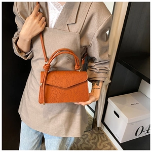 Detail of terracotta lace-embossed square bag with knot handle and slim strap for women