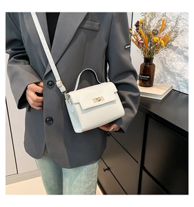Detail of cream white textured crossbody bag with gold buckle on a gray blazer model