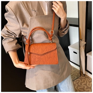 Detail of orange-brown handbag with floral lace embossing and twisted knot handle
