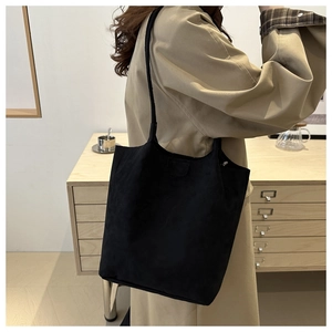 Detail of a black large capacity tote bag in matte suede shown on a model's shoulder