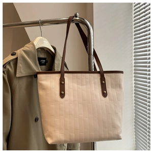 Close-up of woven beige tote bag with brown straps and golden rivets on hanger