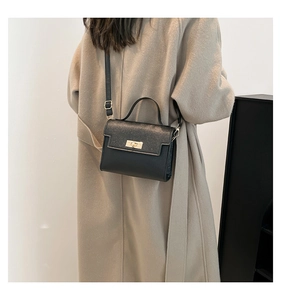 Detail of a vintage-style black leather shoulder bag featuring a gold turn-lock closure