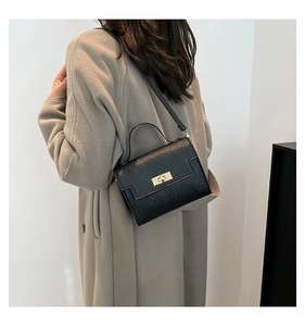 Detail view of a black structured crossbody bag with gold square twist lock on grey coat