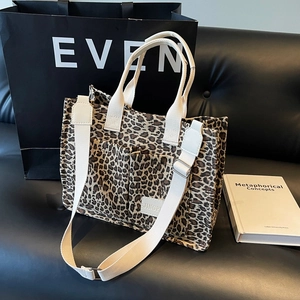 Leopard print canvas tote bag with adjustable strap and dual front pockets on a black sofa