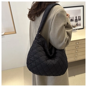 Detailed view of black quilted crossbody bag with wide shoulder strap worn by model