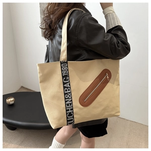 Détail du sac fourre-tout en toile montrant la poche zippée en cuir et la bandoulière