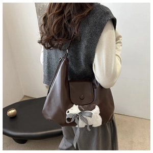 Detail of dark brown leather tote bag with plush dog patch and plaid bow design
