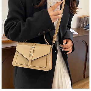 Detail view of khaki pebbled leather crossbody bag with gold buckle on a model