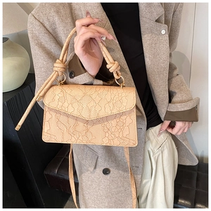 Detail showing elegant lace embossed texture and knotted handle on beige crossbody bag