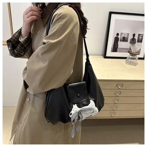 Detail of black faux leather tote with plush dog charm and bow on minimalist background