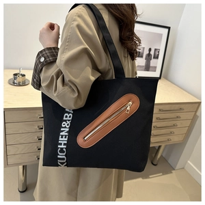 Détail du cabas en toile noire avec fermeture éclair en cuir marron et sangle logotypée