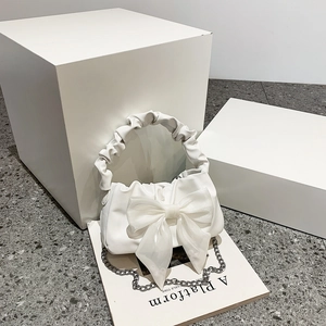 White pleated cloud handbag with large bow and chain strap on minimalist background