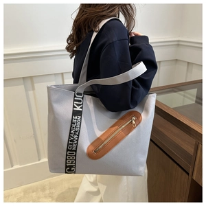 Détail d'un sac cabas gris avec poche en cuir marron et bandoulière à lettres design