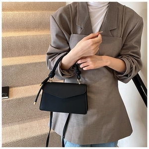 Close-up of black envelope bag featuring litchi texture and knotted woven handle detail