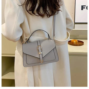Litchi texture handbag in light grey with gold hardware worn on a white coat