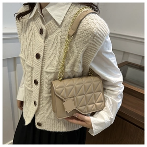 Détail du sac bandoulière matelassé beige avec chaîne dorée sur une tenue chic