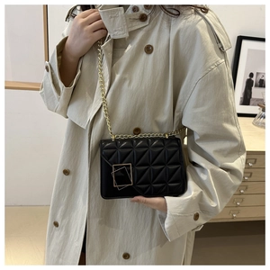 Gros plan du sac à bandoulière noir matelassé avec chaîne dorée porté sur un trench-coat