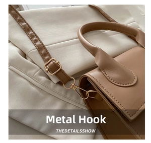 Macro shot of light gold metal hooks and adjustable strap buckle on a leather bag