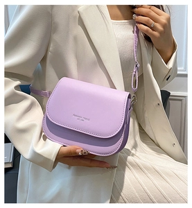 Détail du sac de selle lavande avec inscription tendance porté sur un blazer blanc
