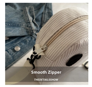 Gros plan du zip sur un petit sac rond en velours côtelé beige à texture rayée