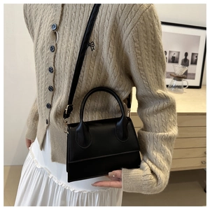 Model showing a black leather square bag with gold hardware in a home setting