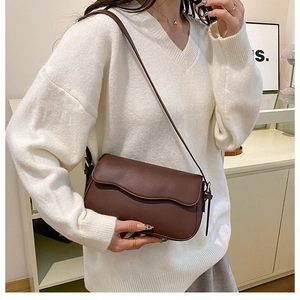 Detail of a brown shoulder bag with a unique wavy edge flap and slim leather strap