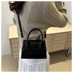 Structured black crossbody bag worn by a model with gold metal buckles and a top handle
