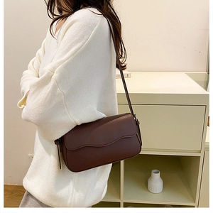Detail of minimalist dark brown leather crossbody bag with unique wavy edge flap design