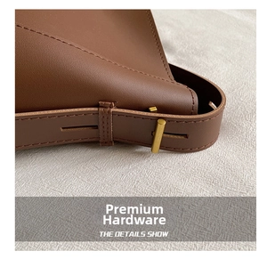 Detail of dark brown leather bucket bag showing stitching and golden metal buckle hardware